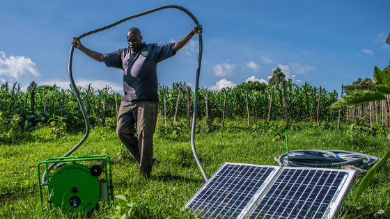 A Kenyan farmer carrying the hose of his solar water pump in Kisumu county