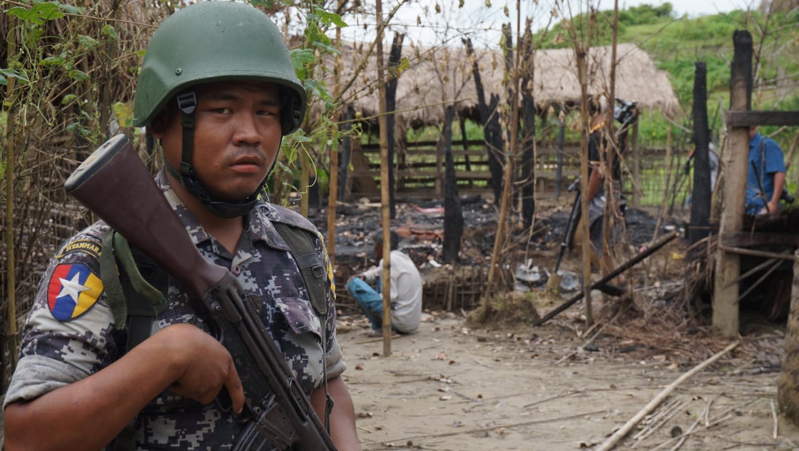 A Myanmar border guard police officer stands guard in front of the remains of a house burned down in a clash between suspected militants and security forces