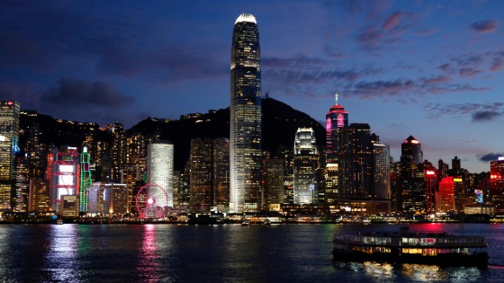 A Star Ferry boat crosses Victoria Harbour in front of a skyline of buildings during sunset in Hong Kong