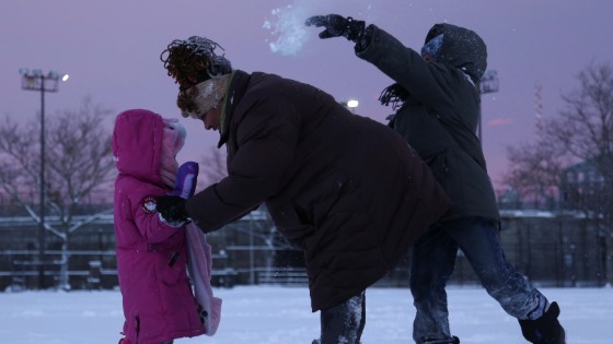 A boy throws snow at his mother as they play in a playground in Harlem