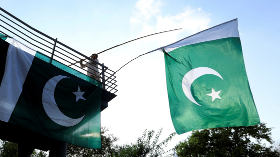 A boy uses a bamboo stick to adjust Pakistani national flags at an overhead bridge