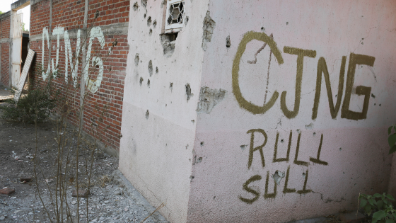 A bullet-riddled facade with the acronym of the Jalisco New Generation Cartel is pictured in El Aguaje