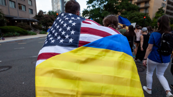 A couple wears a flag that combines the American and Ukrainian flags during a march celebrating Ukraines Independence Day