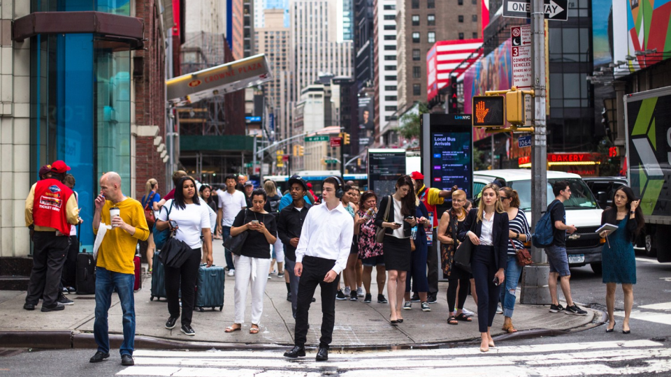 A crowd of people at a crosswalk in New York City.