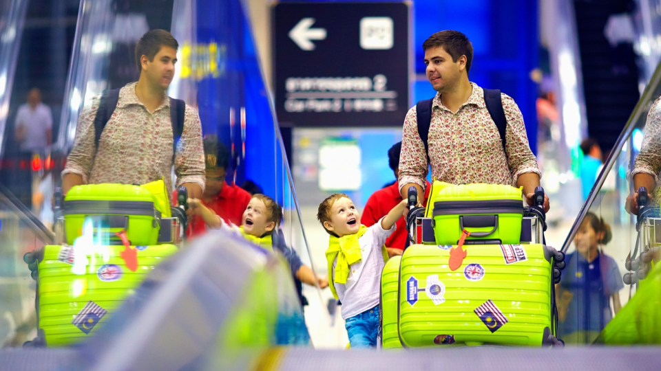 A father carries his familys luggage at an airport.