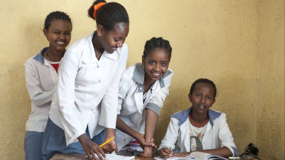 A female teacher and female students gather around a desk