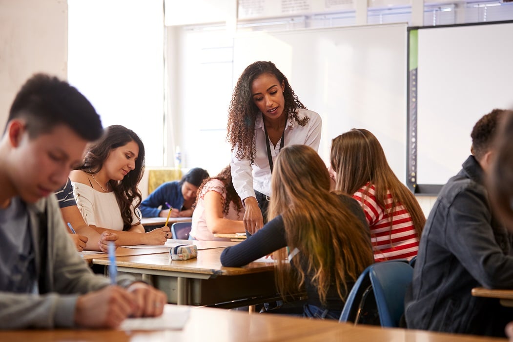 A female teacher assists students with their work in classroom.