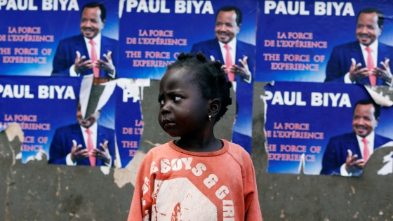 A girl stands near a wall covered with Placards of Cameroon President Paul Biya