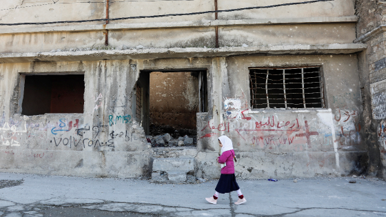 A girl walks near a building destroyed during past fighting with Islamic State militants