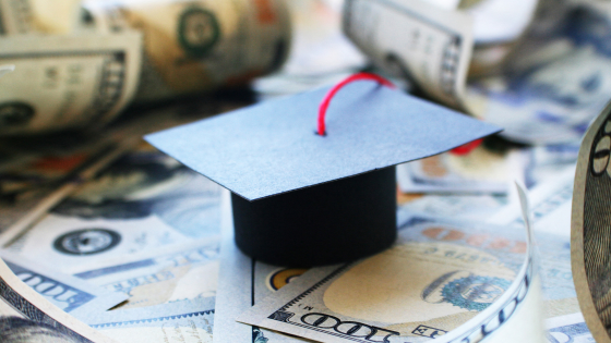 A graduation cap sits on a pile of 100 dollar bills