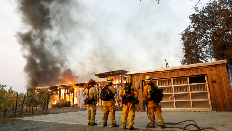 A group of firefighters look on as a house burns during the wind-driven Kincade Fire in Healdsburg, California