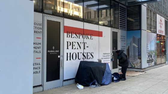 A homeless male in Downtown Chicago next to a sign advertising penthouses.