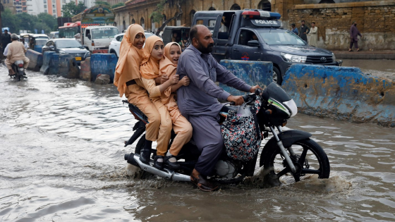 A man and students ride on a motorcycle on a flooded road following rains during the monsoon season in Karachi