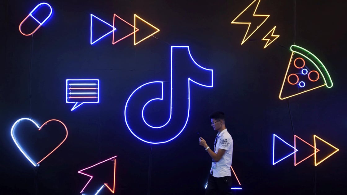 A man holding a phone walks past a sign of Chinese company app TikTok