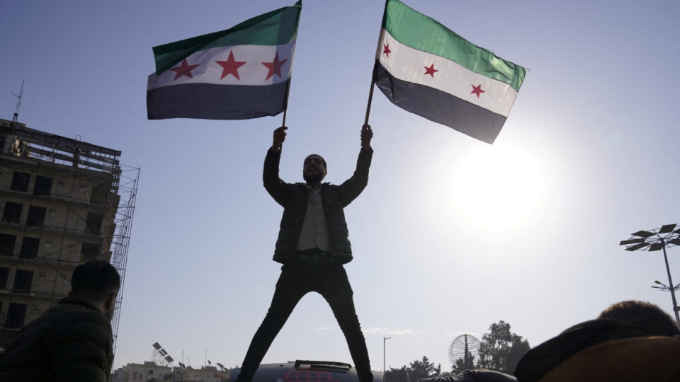 A man holds Syrian opposition flags as he celebrates after Syrias army command notified officers on Sunday that President Bashar al-Assads 24-year authoritarian rule has ended