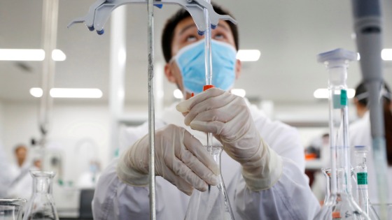 A man wearing gloves and a mask works in a Chinese lab developing an experimental vaccine