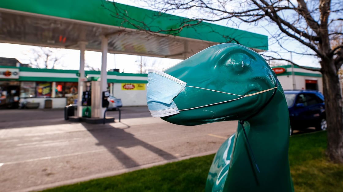 A medical mask covers a fiberglass dinosaur outside of gas station in Denver Colorado