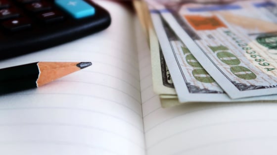 A notebook with a calculator, pencil, and dollar bills