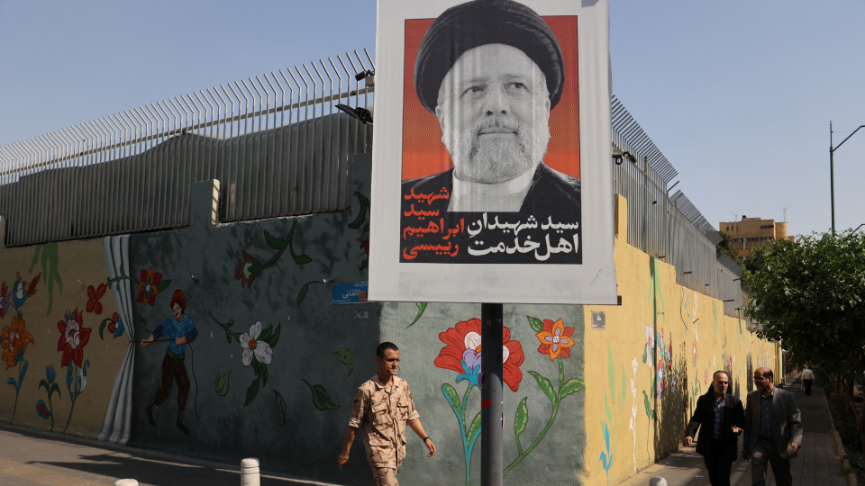 A person walks past a banner with a picture of Irans late president, Ebrahim Raisi, on a street in Tehran