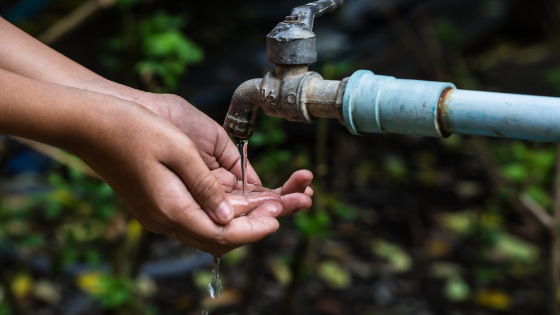 A person washes their hands using water from an outdoor pump