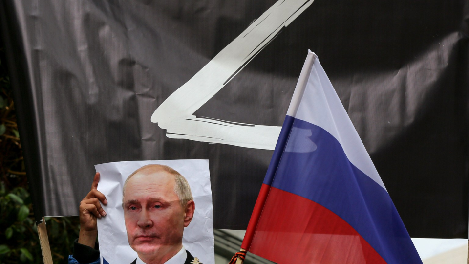 A picture of Vladimir Putin is held up next to a Russian flag.