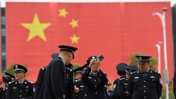 A police officer in front of a giant Chinese flag takes pictures with a mobile phone