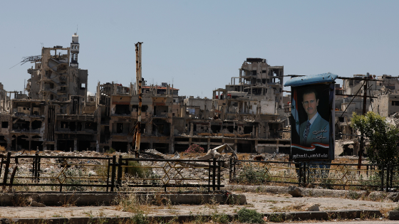 A poster depicting Bashar al-Assad is pictured near damaged buildings