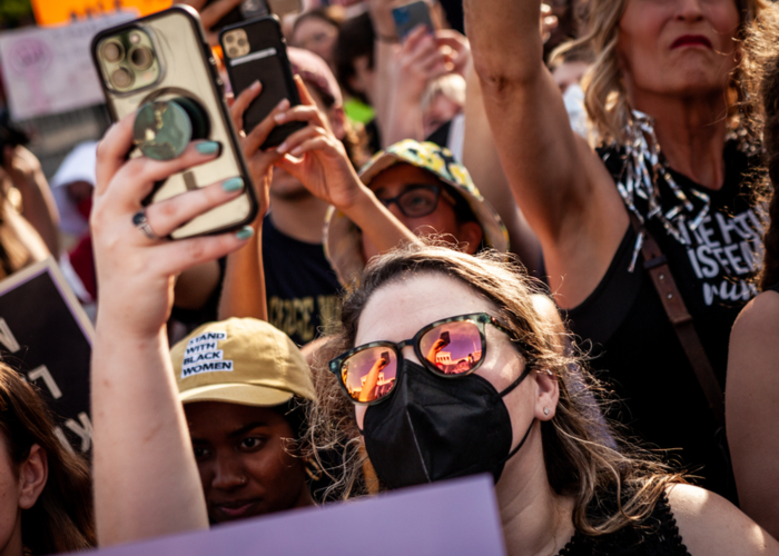 A pro-choice demonstrators sunglasses reflect her taking a photo and the facade of the Supreme Court