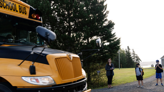 A school bus passes by as Monica Lee, Ronan Lee and Braydon Lee await their turn to load the bus