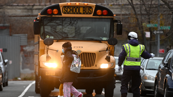 A school crossing guard stops a bus as a woman and child cross the street