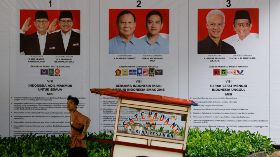 A street vendor pulls his cart past a banner showing presidential candidates contesting the upcoming general election in Jakarta, Indonesia