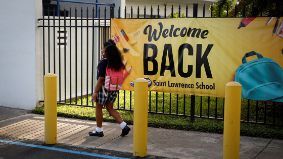 A student wearing a protective mask walks past a welcome back banner on the first day of school