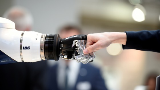 A visitor fist bumps a humanoid robot at the booth of IBG at Hannover Messe