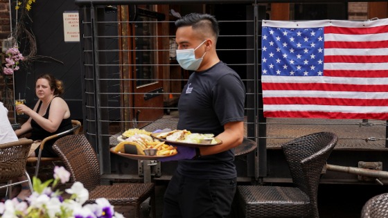 A waiter in a mask serves diners seated outdoors at a restaurant in Alexandria