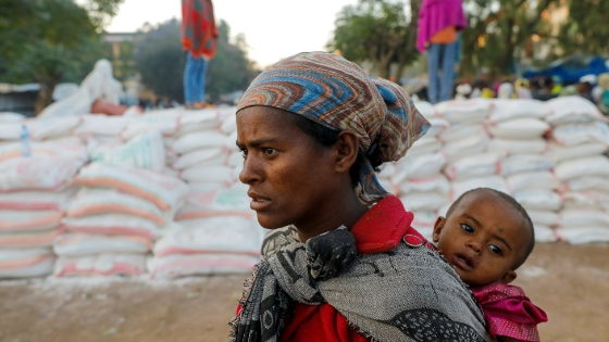 A woman carries an infant as she queues in line for food, at the Tsehaye primary school