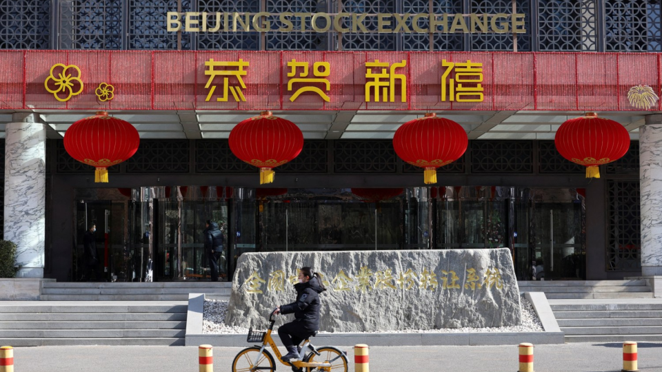 A woman cycles past the Beijing Stock Exchange building adorned with Lunar New Year decorations, on the Financial Street in Beijing, China, February 8, 2024.