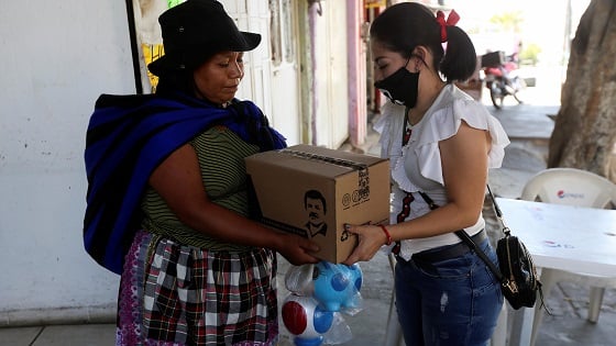 A woman hands out a box with food, face masks and hand sanitizer to an elderly woman.