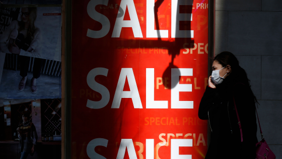 A woman holding her mobile phone walks past a sales advertisement poster in front of a shoe store in Tokyo