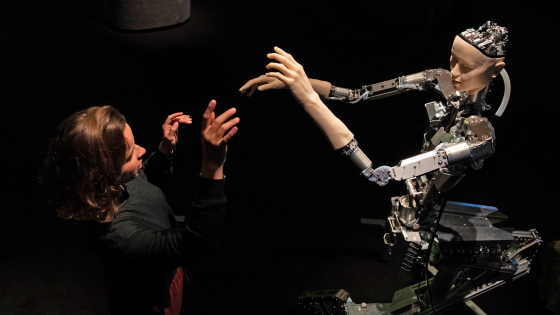 A woman interacts with Alter, a machine with a human-like face and hands who learns through interplaying with the surrounding world