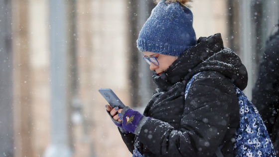 A woman scrolls on her phone during a snowfall