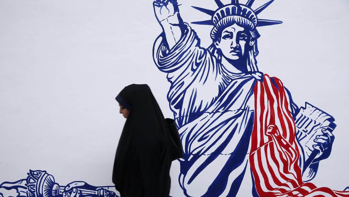 A woman walks in front of new murals of the former US embassy in Tehran