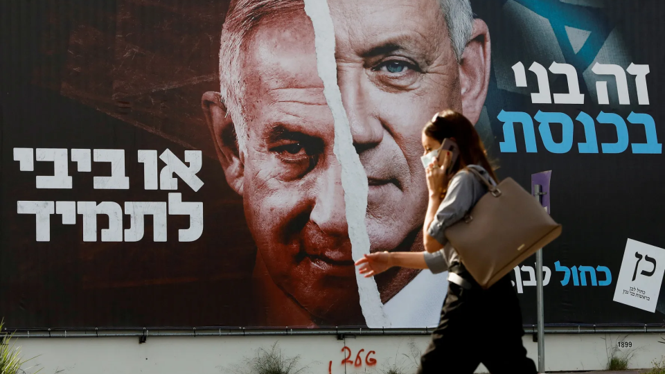 A woman walks past a Blue and White party election campaign banner depicting its leader, Israeli Defense Minister Benny Gantz, alongside Israeli Prime Minister Benjamin Netanyahu.