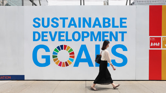 A woman wearing a mask walks past a sign advertising the sustainable development goals