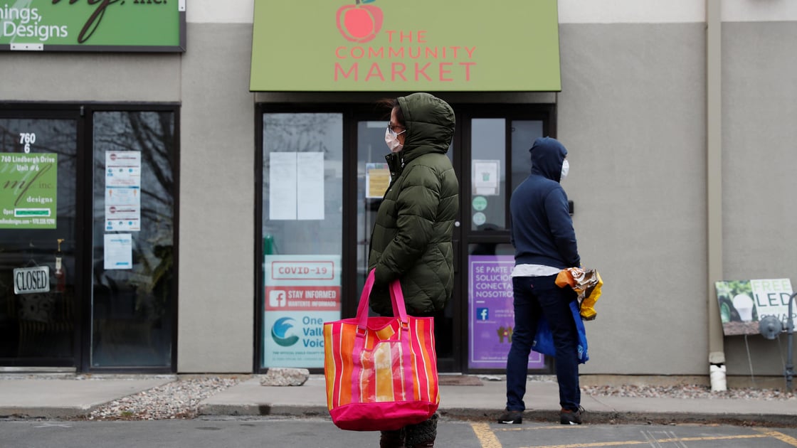 A woman with a face mask practices social distancing while waiting for food donations outside a food bank