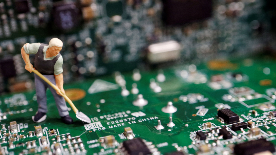 A worker miniature is placed among printed circuit boards with semiconductor chips