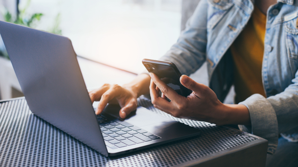 A worker sits at a desk with a laptop and smartphone