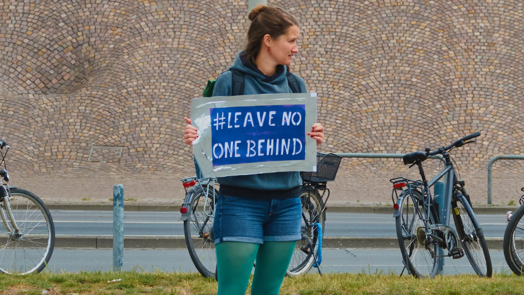 A young woman holds a sign with the text Leave no one behind