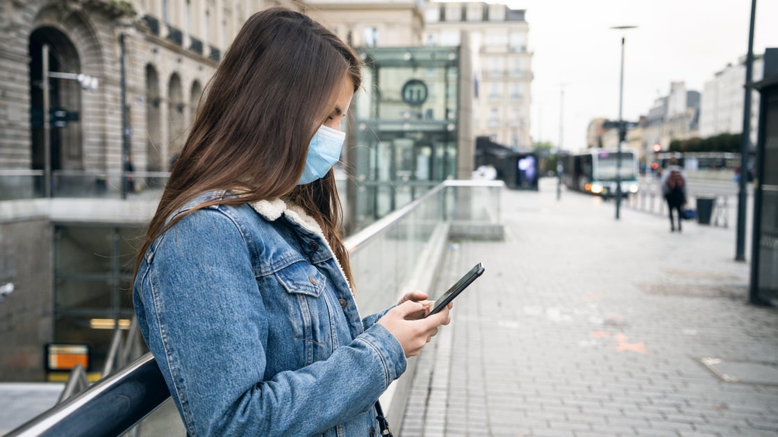 A young woman in a mask is looking at her cell phone in Rienes