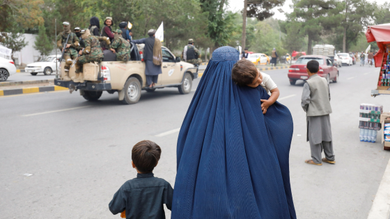 An Afghan woman walks with her children on the anniversary of the fall of Kabul on a street in Kabul