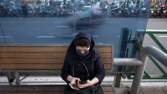 An Iranian woman wearing a protective face mask uses her smartphone